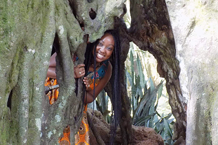 A woman in an orange dress peering out from behind a tree.