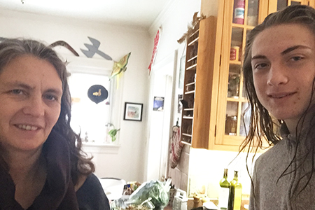 Two people smiling in front of a kitchen counter and cupboards.