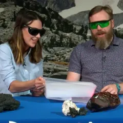 Geologist Ben Andrews and Maggy Benson at a table doing a demonstration with a tray of dry ice while wearing protective glasses.