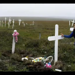 A person in a blue jacket standing in a cemetery marked with white crosses