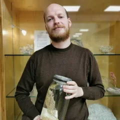 Declan Morrisey smiling for a portrait photo and holding a jarred invertebrate specimen