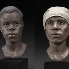 Realistic sculptures of two faces of African descent, one male and one female. The female is wearing a beige head scarf.