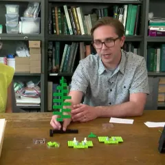Maggy Benson and Dr. Eric Schuettpelz sit at a table with green Legos and a microscope for their discussion of fern life cycles.