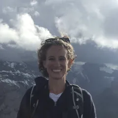 A smiling woman with clouds and mountains behind her