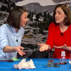 Maggy Benson and Dr. Cara Santelli at a table with examples of minerals and flasks of bacteria that can break down minerals.