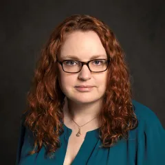 A red-haired woman with light skin tone in a teal shirt
