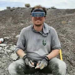 man in grey shirt sitting in rock pile with goggles