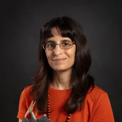image of woman with long dark hair wearing glasses and red shirt holding toy pteranodon