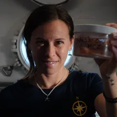 Paula Rodriguez Flores smiling and holding up a container of specimens