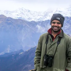 Ornithologist Sahas Barve standing in front of several mountain ridges in the Himalayas