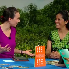 Maggy Benson and Dr. Gabriela Pérez Báez sit at a table with several colorful pictures and brochures.