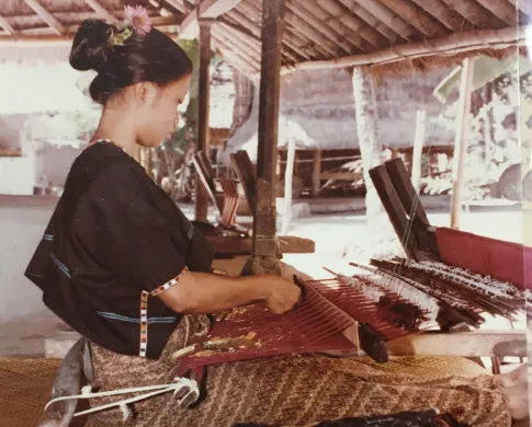A woman outside in Indonesia working a textile loom 