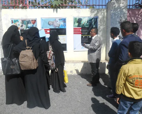 A group of people look to posters on a garden wall 