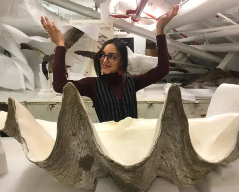 Odalys Lugo Morales holding her hands up, gesturing at items around her in the attic of the Natural History Museum.