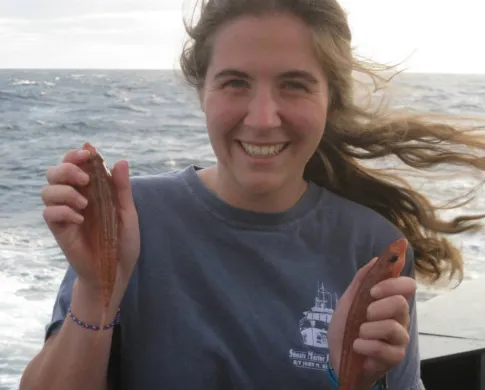 Ichthyologist Kate Bemis holding two small fish while standing on a boat in the ocean.