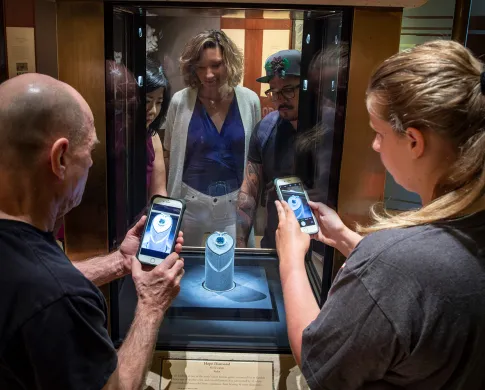 Two visitors standing in front of the case holding the Hope Diamond, holding up their smart phones to take a picture of it.