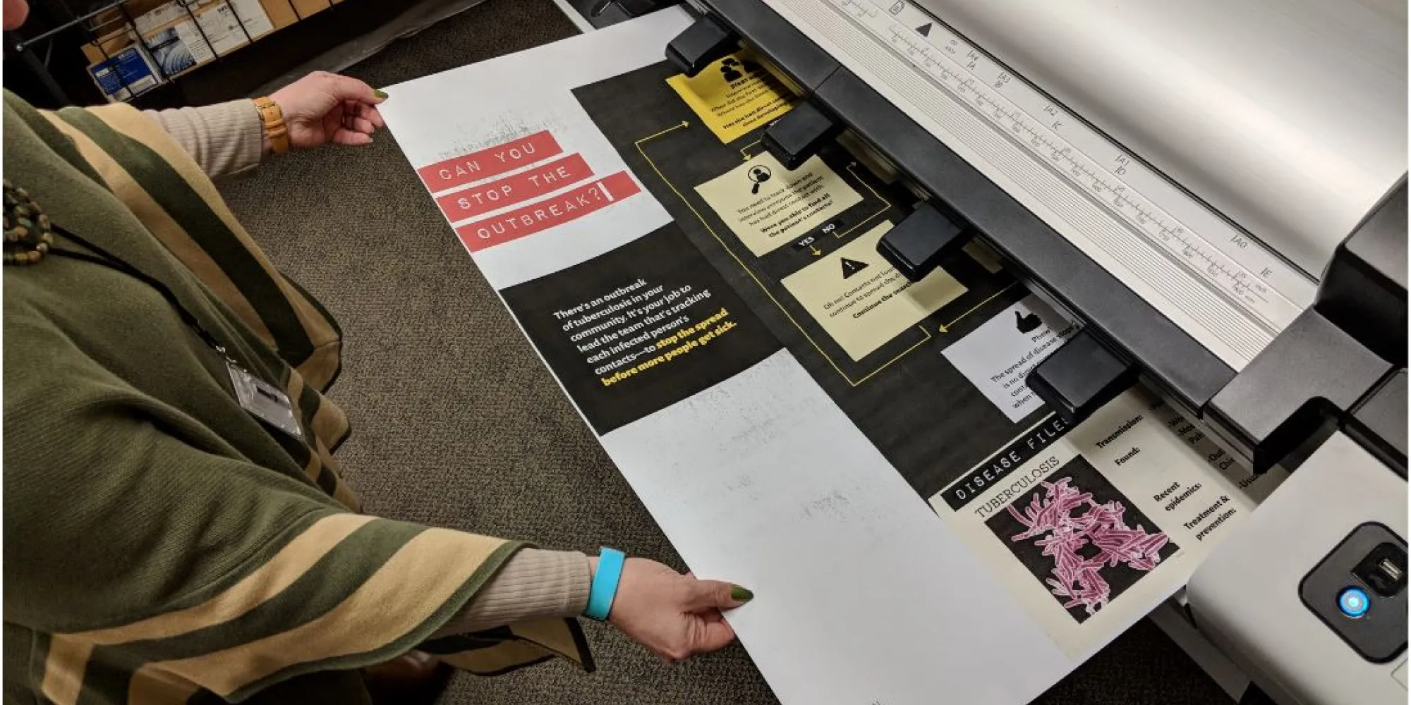 A large poster coming out of a printer being grabbed by two hands 