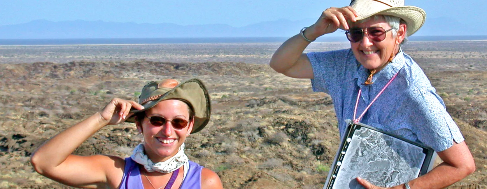 Photo of two women looking at the camera holding their hats doing fieldwork