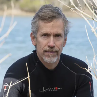 A man in a wetsuit posing in front of a body of water