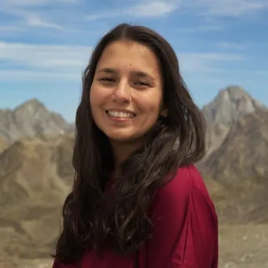 A woman with medium skin tone and long dark hair in front of mountains