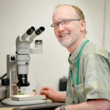 Doctor Neal Woodman, USGS Research Associate, sitting at a microscope 