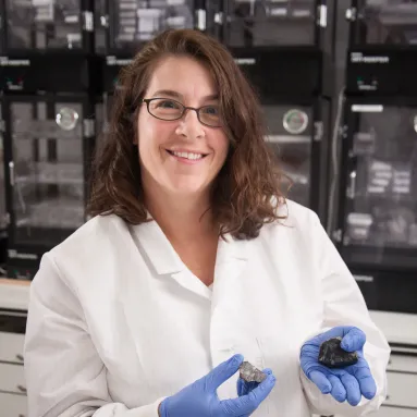 Scientist in lab coat holds two meteorites
