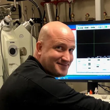 A man with a bald head turns his head and smiles from in front of a computer
