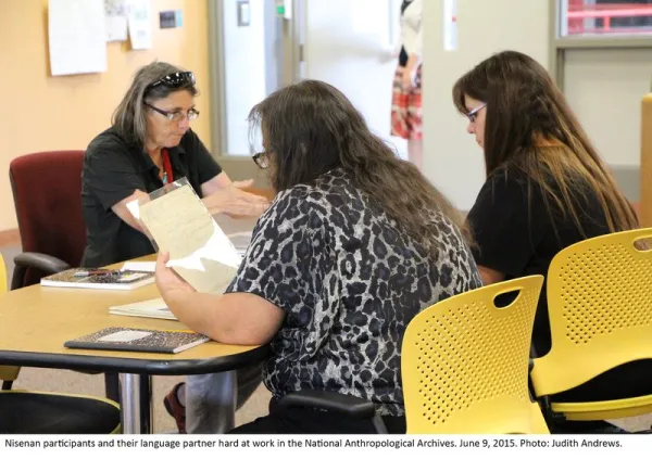 Three people sitting at a table examining archival materials.