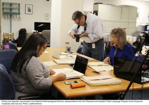 People looking at archival materials; one man taking a photo of documents.