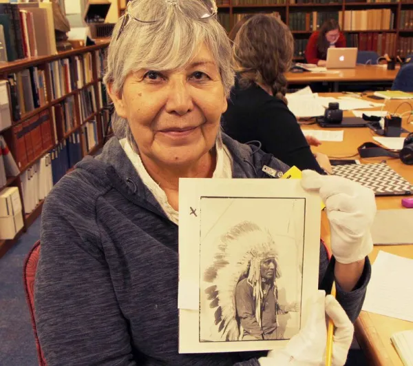 Woman holding an image of her great-grandfather; Native American man in a traditional headdress.