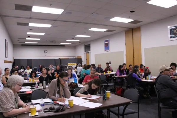 Group of people at separate desks writing notes.