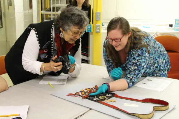 Women examining woven beadwork on a shoulder bag.