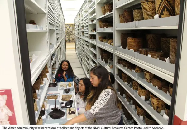 Three people looking at a pulled out drawer, standing between two collections storage units.