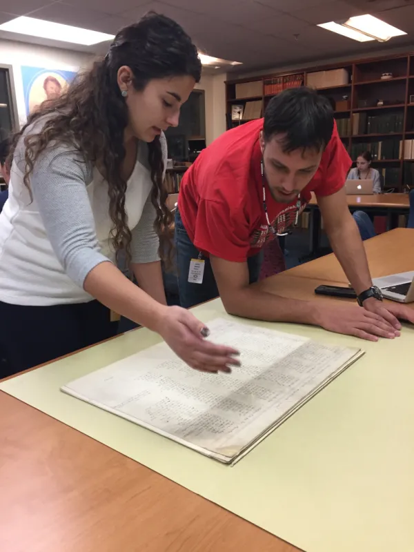 Person referencing archival documents as another looks closely at them.