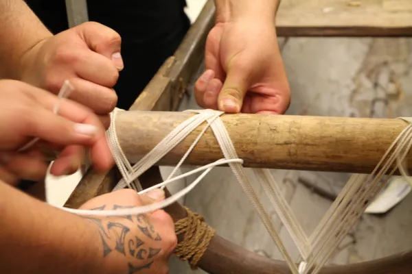 Two pairs of hands tying rope to create a lashing.