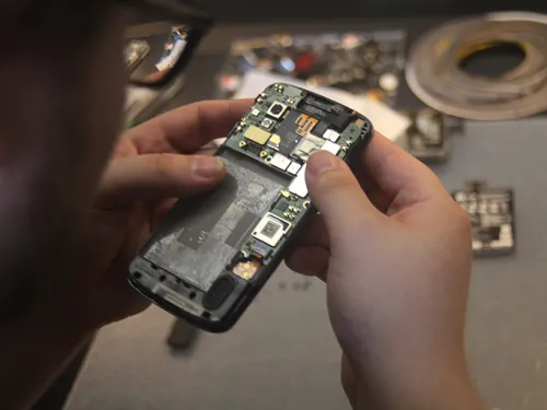 Two hands holding a cellphone that has its back removed, exposing the circuitry and parts.