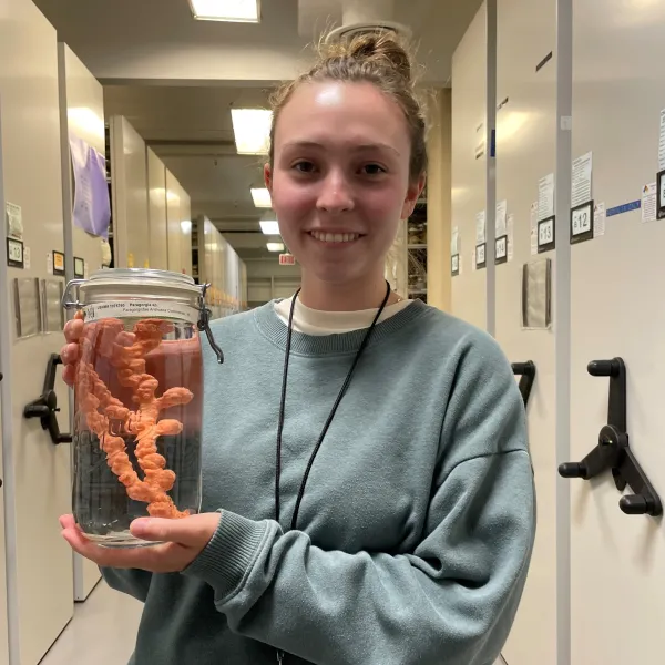 A smiling woman presenting a jar of preserved coral