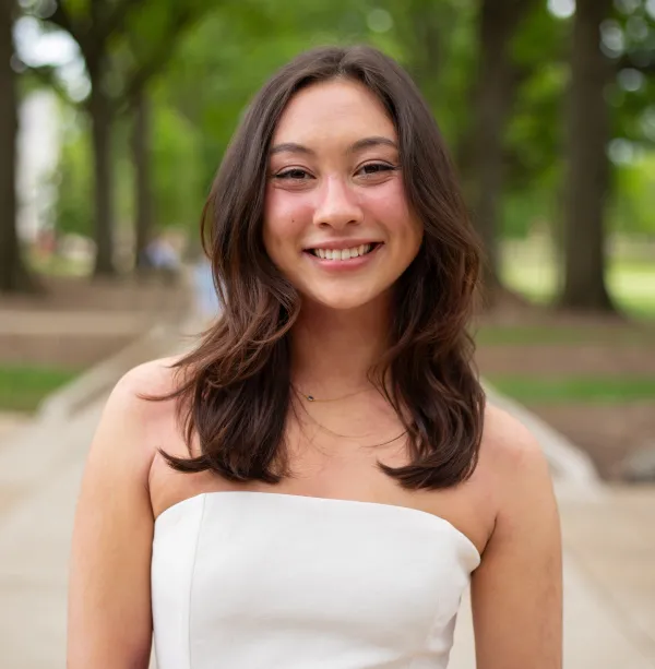 A brown haired woman in a white dress smiling for a photograph against a blurred background
