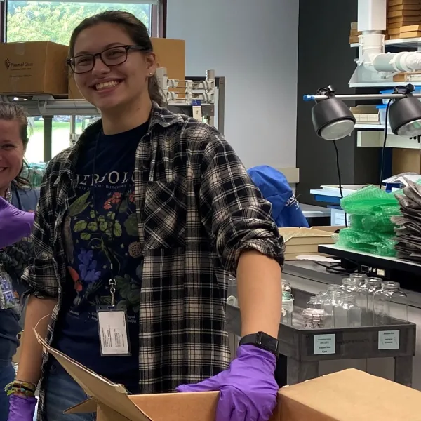 A smiling woman in a laboratory holding a box of specimens