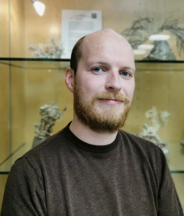 Headshot of Declan Morrisey, posing in front of a glass case of dried specimens