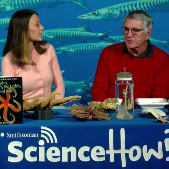 Maggy Benson and Dr. Dave Pawson seated at a table with a number of large specimens and two books.