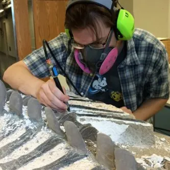 Scientist cleaning bones in dinosaur. He is wearing a respirator mask, earphones, and glasses to protect himself from the dust and noise that this process generates