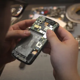 Two hands holding a cellphone that has its back removed, exposing the circuitry and parts.