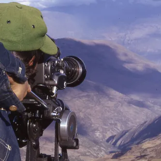 Filmmaker, looking through camera at mountains and a valley