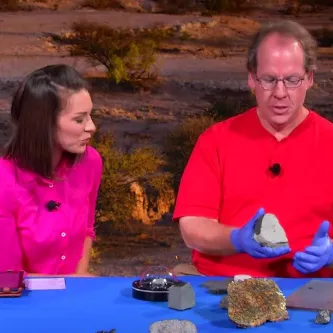 Maggy Benson and Dr. Tim McCoy seated at a table with several different meteorites.