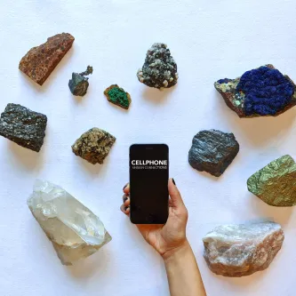 minerals on a white table with a hand holding a smart cellphone in middle with words cellphone unseen connections
