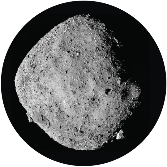 Diamond-shaped gray asteroid with shadows at upper and lower right. Its surface is rough with many small, loose rocks and several large ones.
