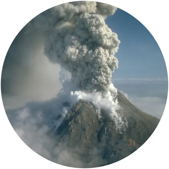A volcano erupts a column of gray ash above it, while white gas flows down its slopes.