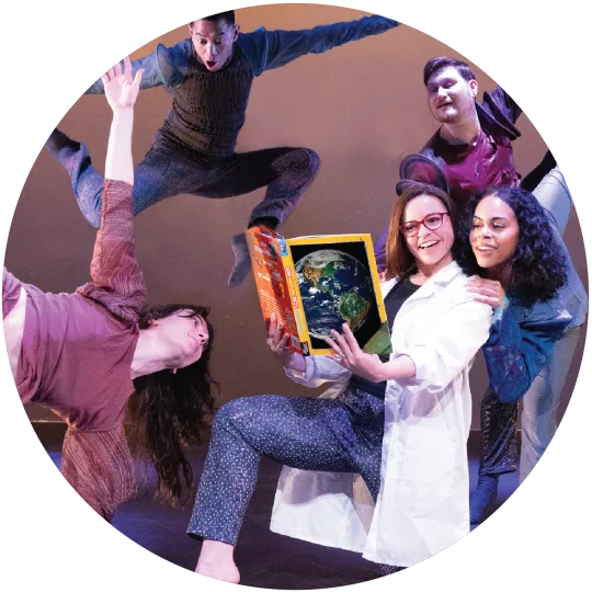 A woman in a white lab coat kneeling on one knee while holding an open book with a picture of planet Earth on the cover. Three dancers pose around her. One looking over her shoulder, another behind her with one arm and leg up in the air, another looking sideways at her, and a fourth in mid-air with arms wide.