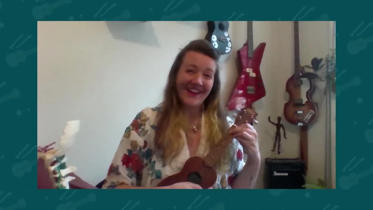 A woman smiling and playing a ukulele.